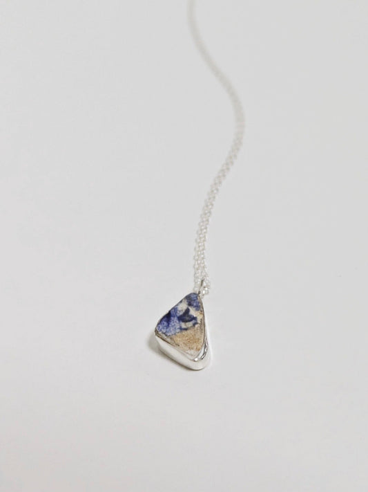 Close up of mini blue and white sea pottery necklace on white background.