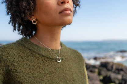 Woman wearing molten silver earrings and necklace with a blurred ocean background