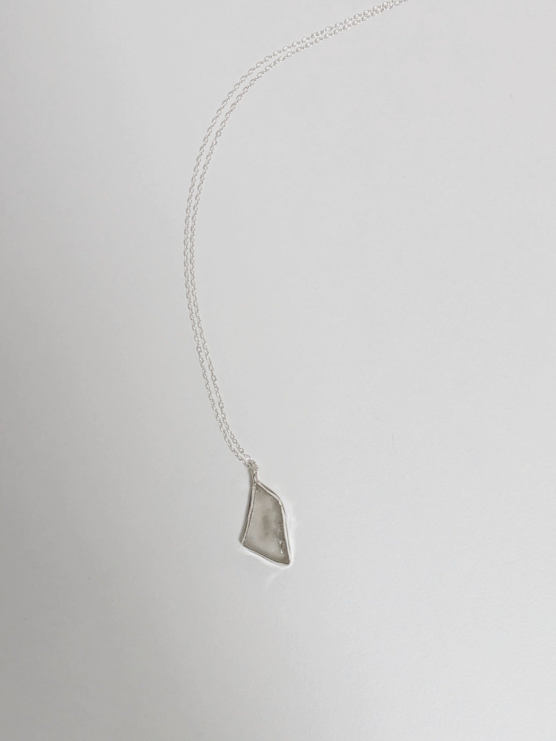 White sea glass pendant on a silver necklace lying on a light grey background