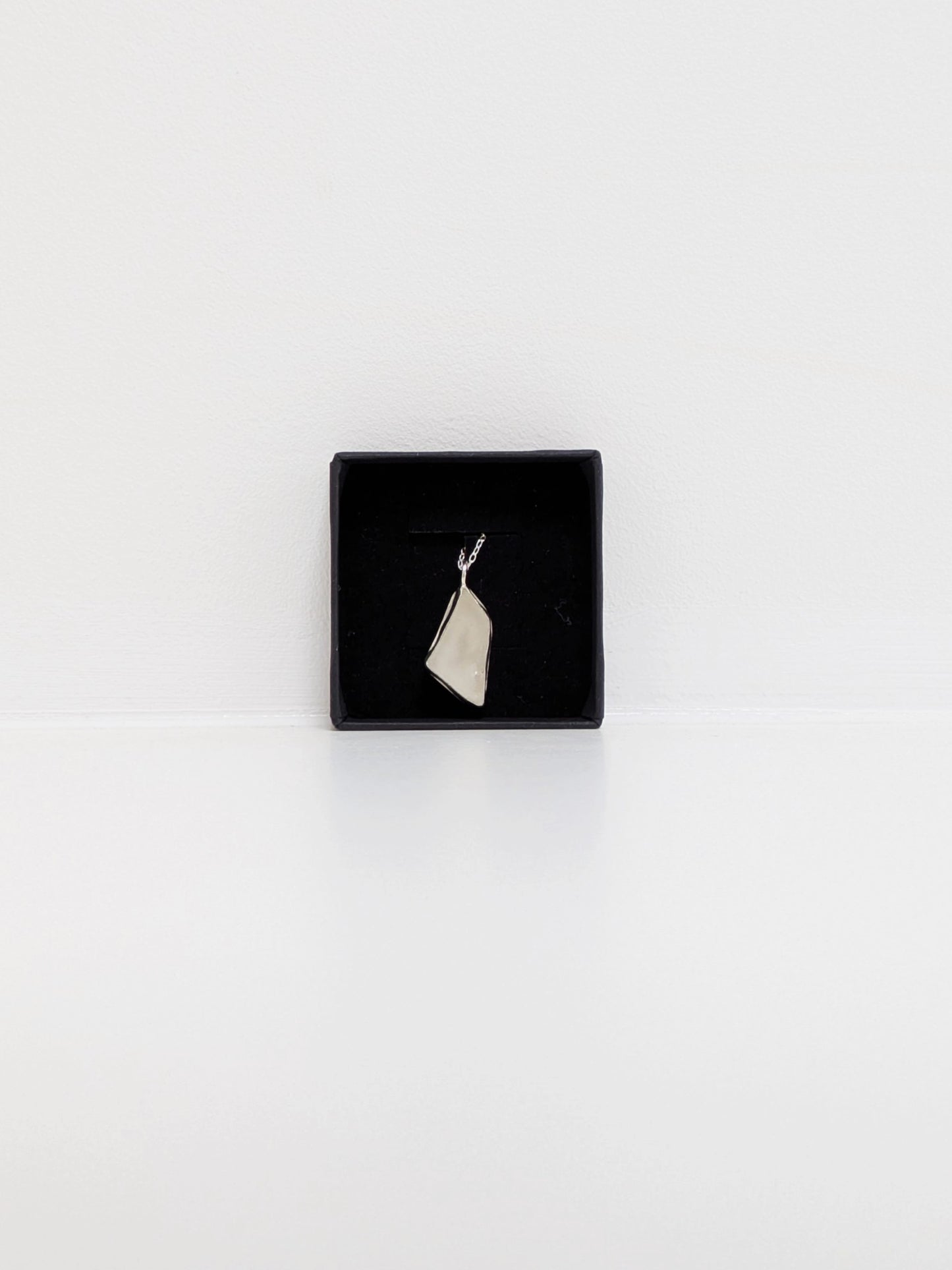 White sea glass pendant in a black jewellery box on a white background