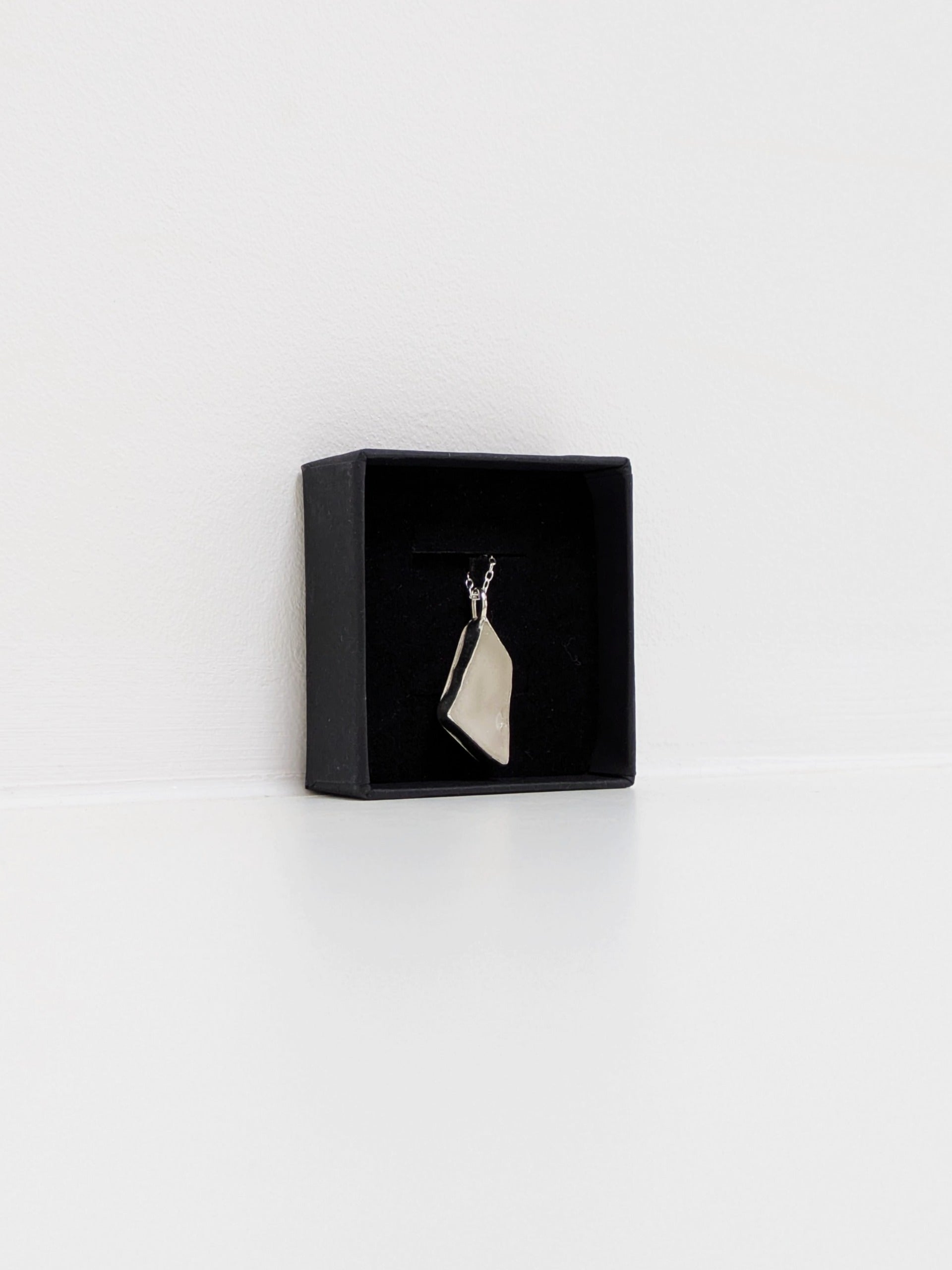 White sea glass pendant on a silver chain in a black jewellery box on a white background