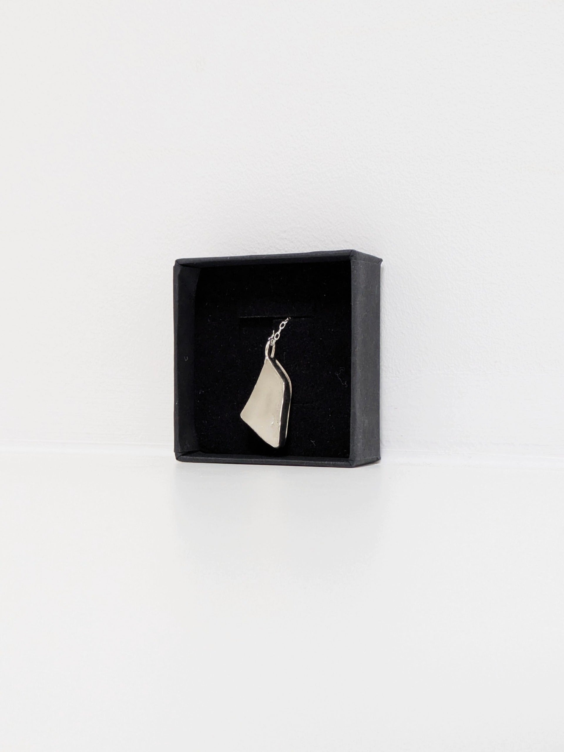 White sea glass pendant in a black jewellery box on a white background