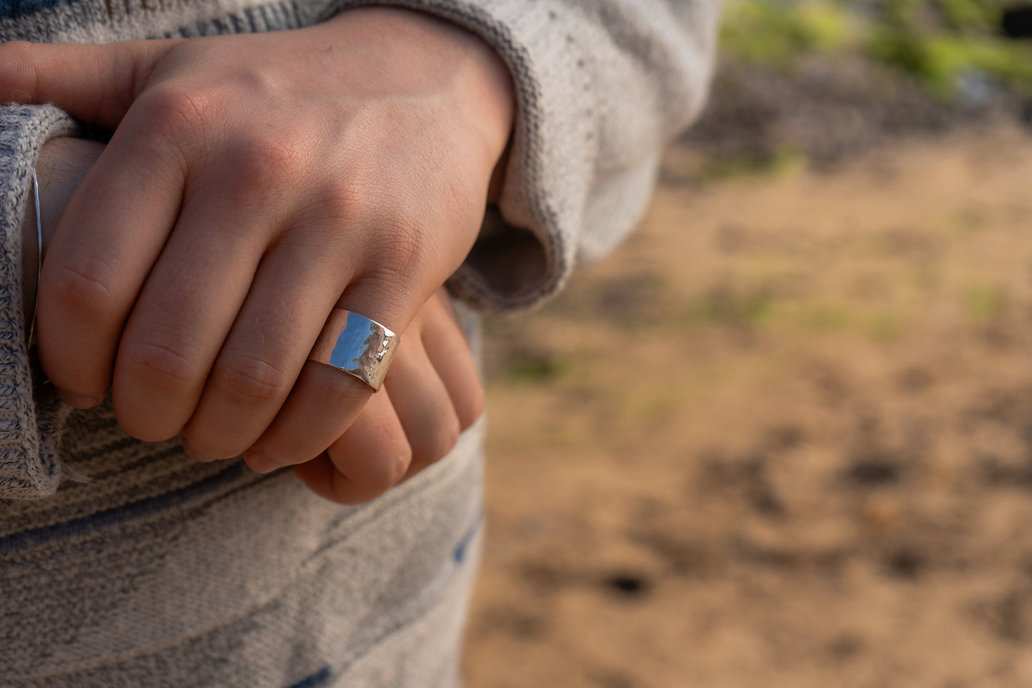 Close-up of a hand wearing a wide hammered ring with a blurred natural background