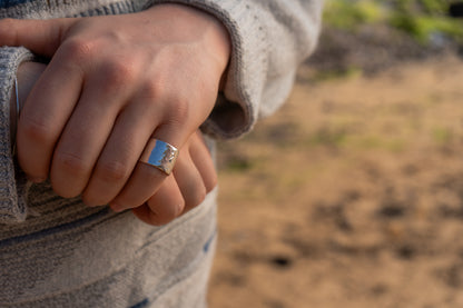 Close-up of a hand wearing a wide hammered ring with a blurred natural background