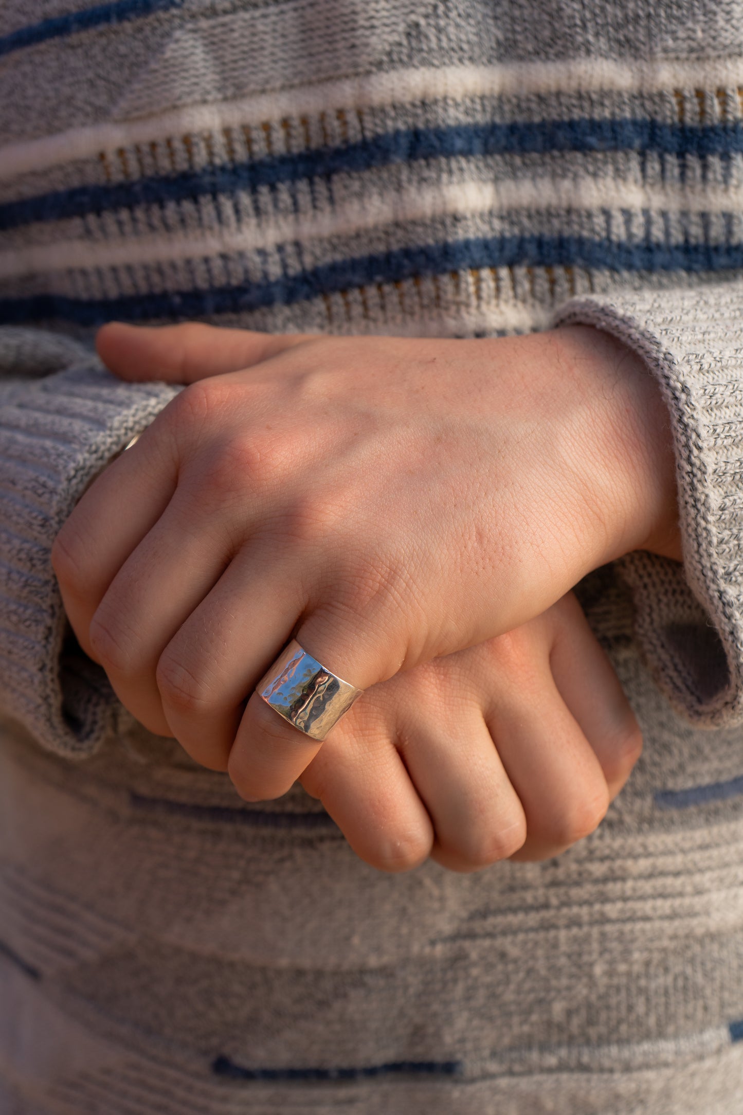 Close-up of a hand wearing a wide hammered ring, held in front of a striped jumper.