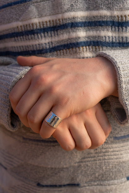 Close-up of a hand wearing a wide hammered ring, held in front of a striped jumper.
